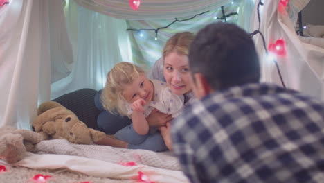 Laughing-parents-with-young-daughter-having-fun-in-homemade-camp-in-child's-bedroom-at-home---shot-on-slow-motion
