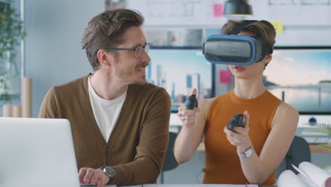 Female-Architect-Wearing-VR-Headset-In-Office-Working-With-Male-Colleague-At-Desk-With-Laptop