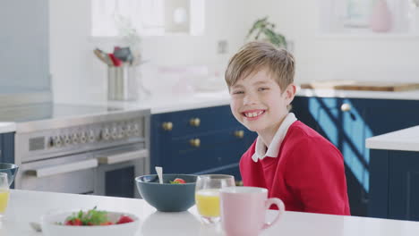 Porträt-Eines-Lächelnden-Jungen-In-Schuluniform,-Der-An-Der-Küchentheke-Frühstückt