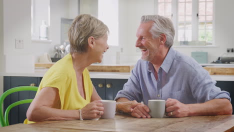 Retired-Couple-Sitting-Around-Table-At-Home-Having-Morning-Coffee-Together