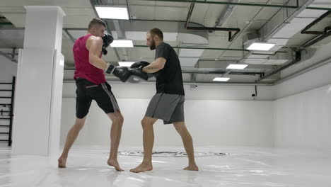 Two-men-in-a-white-gym.-The-coach-and-the-fighter-work-out-the-kick-in-the-jump-knee-on-the-paws-in-slow-motion