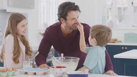 Children-Putting-Cake-Mixture-On-Father's-Nose-In-Kitchen-As-They-Have-Fun-Baking-Cakes-Together