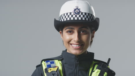 Studio-Portrait-Of-Smiling-Young-Female-Police-Officer-Holding-Helmet-Against-Plain-Background