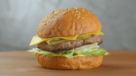 Der-Hamburger-Dreht-Sich-Auf-Einem-Holzbrett.-Ein-Burger-Mit-Schnitzel,-Salat,-Käse-Und-Tomaten-Dreht-Sich-Vor-Einer-Grauen-Wand