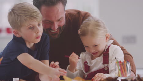 Father-With-Children-At-Home-Doing-Craft-And-Making-Picture-From-Leaves-In-Kitchen