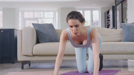 Woman-in-fitness-clothing-at-home-in-lounge-doing-stretches-and-exercising-on-mat---shot-in-slow-motion