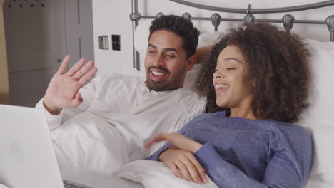 Couple-In-Bed-Wearing-Pyjamas-Having-Video-Chat-On-Laptop-At-Home