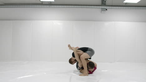 Two-male-wrestlers-in-a-white-room-work-out-throwing-mats.-Take-a-grapple-and-throw-through-yourself.