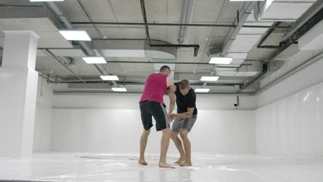 Two-male-wrestlers-in-a-white-room-work-out-throwing-mats.-Take-a-grapple-and-throw-through-yourself.