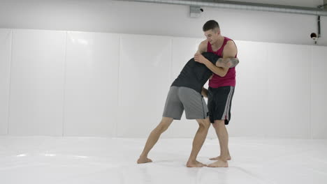 Greco-Roman-wrestlers-in-a-white-room-with-mats.-Practicing-self-defense-techniques.-Throw-and-pain.
