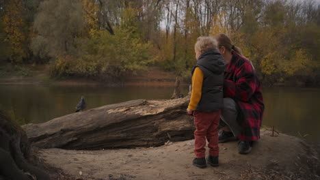 autumn-nature-in-forest-little-child-is-exploring-mother-and-boy-are-playing-with-dove-on-shore-of-lake-having-fun-together-resting-at-weekend