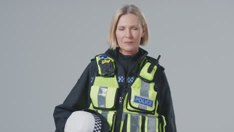 Studio-Portrait-Of-Serious-Mature-Female-Police-Holding-Helmet-Officer-Against-Plain-Background