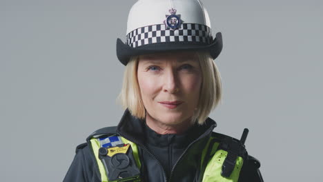 Portrait-Of-Serious-Mature-Female-Police-Officer-Turning-To-Look-At-Camera-On-Plain-Background