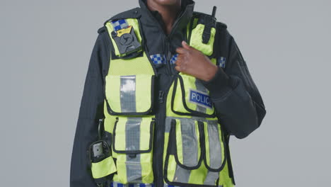 Full-Length-Studio-Portrait-Of-Smiling-Young-Female-Police-Officer-Against-Plain-Background