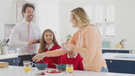 Padres-Ayudando-A-Niños-En-Uniforme-Escolar-A-Prepararse-Mientras-Desayunan-En-El-Mostrador-De-La-Cocina