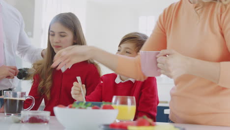 Eltern-Helfen-Kindern-In-Schuluniform-Dabei,-Sich-Fertig-Zu-Machen,-Während-Sie-An-Der-Küchentheke-Frühstücken