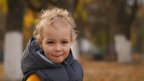 closeup-portrait-of-little-child-with-blonde-curly-hair-in-autumn-park-in-city-funny-face-and-grimacing-of-baby-boy-walking-children