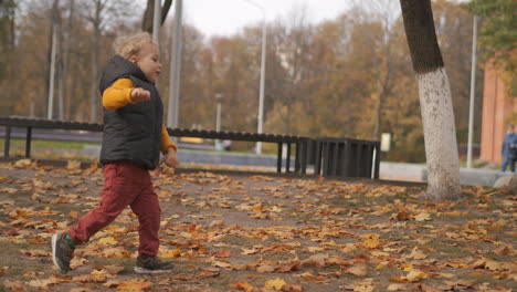 funny-little-boy-is-running-in-park-area-at-autumn-day-having-fun-at-walking-at-weekend-active-rest-of-family-in-city-at-fall-season
