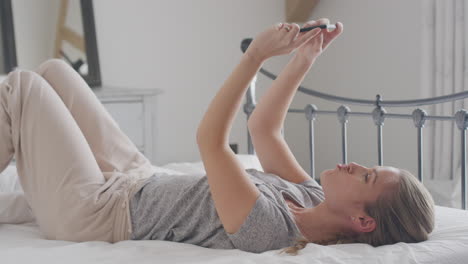 Woman-Wearing-Pyjamas-Posing-And-Taking-Selfies-On-Mobile-Phone-Lying-On-Bed