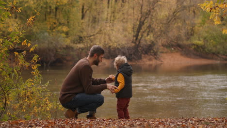 happy-father-is-talking-with-his-child-son-in-forest-standing-on-coast-of-lake-or-river-at-autumn-weekend-family-trip-in-woodand-or-reserve-park