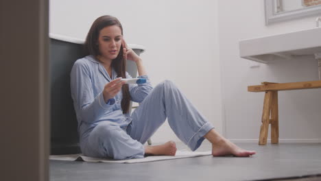 Excited-Woman-Sitting-On-Bathroom-Floor-With-Positive-Home-Pregnancy-Test