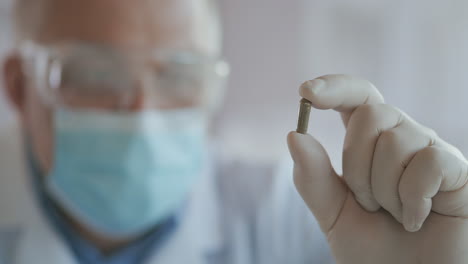 Extreme-close-up-of-scientist-in-the-mask-developer-of-the-vaccine-against-coronavirus-holds-in-his-hands-the-green-one.-The-doctor-looks-at-the-painkillers-antiviral-medication.-Vitamins.-High-quality-4k-footage