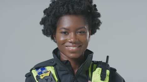 Studio-Portrait-Of-Smiling-Young-Female-Police-Officer-Against-Plain-Background