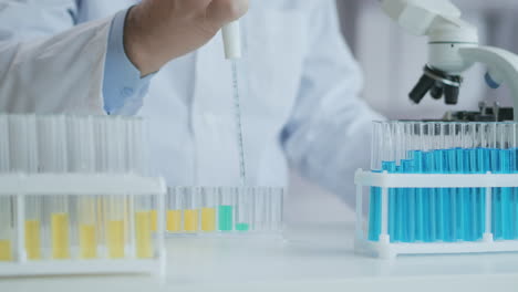 Laboratory.-Hand-in-blue-glove-moves-the-tubes-and-drips-blue-liquid.-Medical-worker-holding-yellow-and-blue-liquid-sample-in-test-tube-analyzing-urine-in-lab.-High-quality-4k-footage