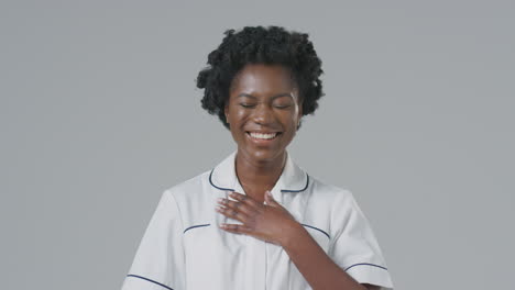 Studio-Portrait-Of-Laughing-Female-Nurse-In-Uniform-Against-Plain-Background