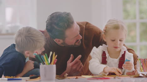 Father-With-Children-At-Home-Doing-Craft-And-Making-Picture-From-Leaves-In-Kitchen