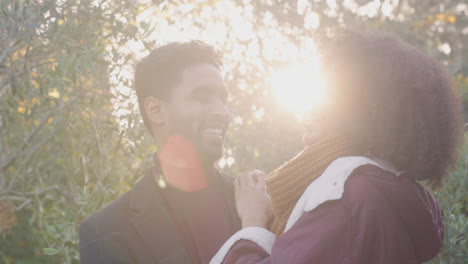 Portrait-Of-Loving-Young-Couple-Hugging-Outdoors-In-Fall-Or-Winter-Countryside-Against-Flaring-Sun
