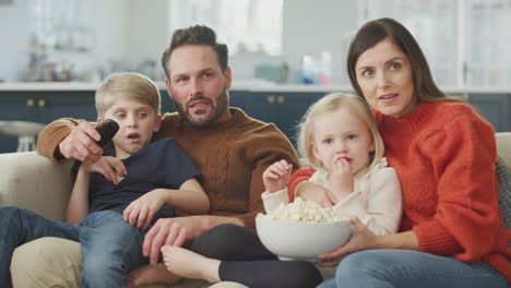 Familie-Sitzt-Mit-Popcorn-Auf-Dem-Sofa-Und-Schaut-Sich-Gemeinsam-Einen-Gruselfilm-Im-Fernsehen-An