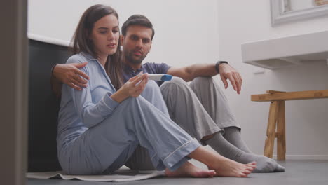Enttäuschtes-Paar-Sitzt-Zu-Hause-Im-Badezimmer-Auf-Dem-Boden-Und-Hat-Einen-Negativen-Schwangerschaftstest