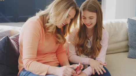 Mother-And-Daughter-Having-Fun-Sitting-On-Sofa-At-Home-Doing-Nails-Together