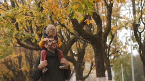 idyllic-family-walk-in-forest-at-autumn-little-boy-is-sitting-on-shoulders-of-his-dad-father-and-son-are-having-fun-and-laughing-happiness-and-harmony