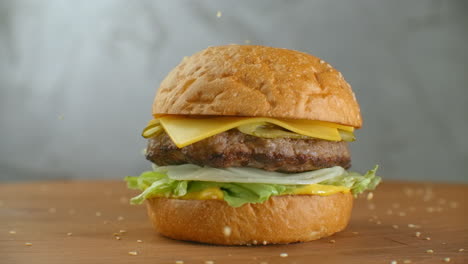In-slow-motion-sesame-seeds-fall-on-a-spinning-hamburger.-Hamburger-on-a-wooden-Board