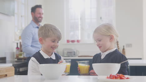 Zwei-Kinder-In-Schuluniform-Frühstücken-In-Der-Küche,-Während-Sich-Der-Vater-Für-Die-Arbeit-Fertig-Macht