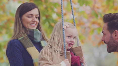 Parents-Pushing-Daughter-And-Having-Fun-On-Rope-Swing-In-Autumn-Garden