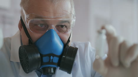 Extreme-Close-up-of-a-scientist-in-a-blue-respirator-and-protective-glasses-who-developed-a-coronavirus-vaccine-holding-an-ampoule-of-white-powder.-Narcotic-substances-and-painkillers.-High-quality-4k-footage