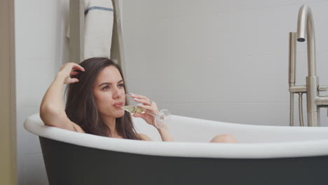 Woman-Lying-And-Relaxing-In-Bath-At-Home-Drinking-Glass-Of-Wine