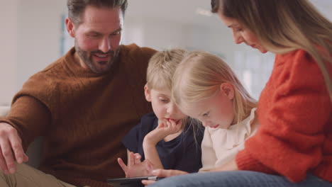 Smiling-Family-Sitting-On-Sofa-Having-Fun-Using-Digital-Tablet-Together