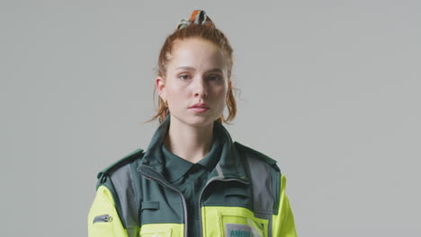 Studio-Portrait-Of-Serious-Young-Female-Paramedic-Turning-To-Face-Camera-Against-Plain-Background