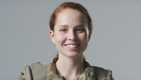 Studio-Portrait-Of-Smiling-Young-Female-Soldier-In-Military-Uniform-Against-Plain-Background