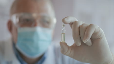 Close-up-of-the-developer-of-the-coronavirus-vaccine-holding-an-ampoule-of-white-liquid-examining-and-holding-the-vaccine-in-gloves.-High-quality-4k-footage