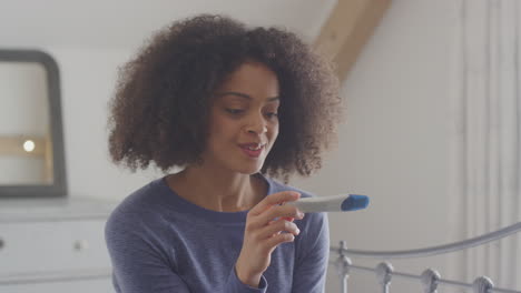 Excited-Woman-Sitting-On-Bed-In-Bedroom-With-Positive-Home-Pregnancy-Test