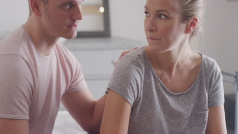 Disappointed-Couple-Sitting-On-Bed-At-Home-With-Negative-Home-Pregnancy-Test