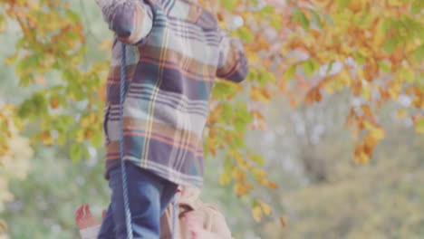 Close-Up-Of-Brother-And-Sister-Having-Fun-On-Rope-Swing-In-Autumn-Garden