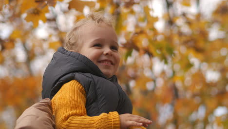 Glückliches-Kind-Sitzt-Auf-Den-Schultern-Der-Eltern-Beim-Spaziergang-Im-Park-Im-Herbst-Nahaufnahme-Porträt-Eines-Kleinen-Lächelnden-Jungen-Glückliches-Familienwochenende-In-Der-Natur