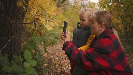 Mutter-Bringt-Seinem-Kleinen-Sohn-Bei,-Mit-Dem-Smartphone-Fotos-Zu-Machen,-Ein-Familienausflug-In-Die-Natur-Im-Herbstlichen-Wald-Oder-Park,-Kindheit-Und-Mutterschaft