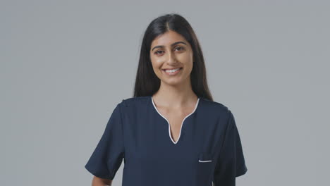 Studio-Portrait-Of-Smiling-Female-Nurse-In-Uniform-Against-Plain-Background